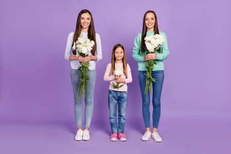 Photo of shiny cute mommy two daughters wear casual pullovers holding white flowers smiling isolated violet color backgroundの写真素材
