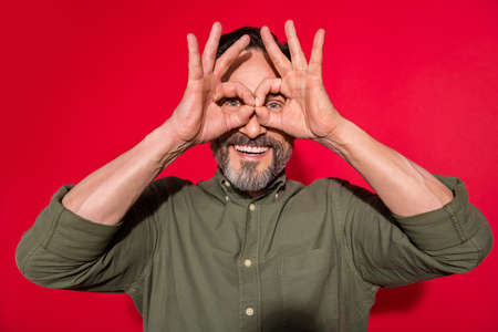 Photo portrait man wearing casual clothes fooling showing binocular with fingers isolated vivid red color backgroundの写真素材