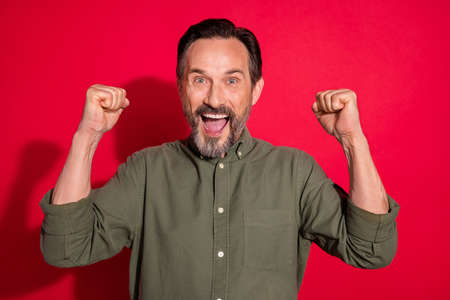 Photo portrait businessman wearing green shirt gesturing like winner isolated bright red color backgroundの写真素材