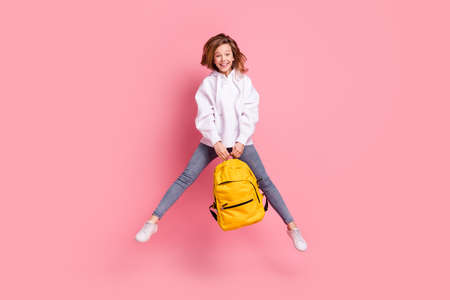 Full length body size girl jumping up keeping schoolbag happy cheerful isolated pastel pink color...