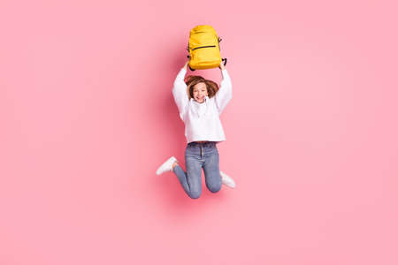 Full length body size girl jumping high keeping schoolbag over head isolated pastel pink color backgroundの写真素材