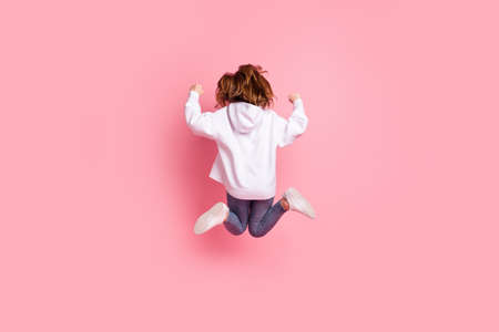 Full length body size back view girl jumping high gesturing like winner in white hoodie isolated pastel pink color backgroundの写真素材