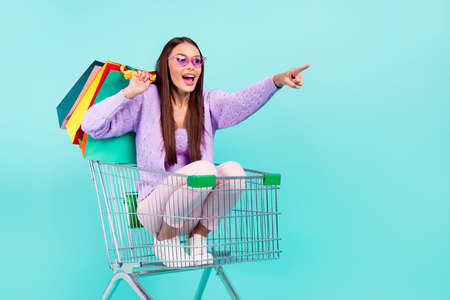 Photo of excited lady sit cart carry bags ride finger empty space wear sunglass shirt isolated teal color backgroundの写真素材