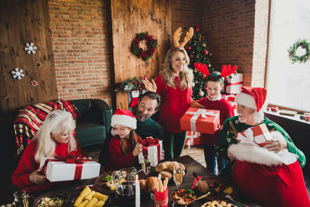 Photo of little childhood grandchildren pensioner retired friends noel people dinner table open gifts santa claus hats xmas indoors houseの写真素材