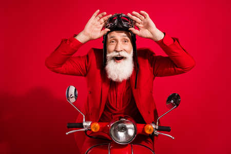 Photo of pretty impressed age gentleman wear new year costume headwear riding motorcycle arms eyewear isolated red color backgroundの写真素材