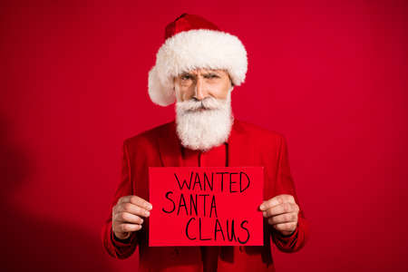 Photo of retired pensioner bearded old man hold hands wanted santa claus card bad mood xmas isolated on red color backgroundの写真素材
