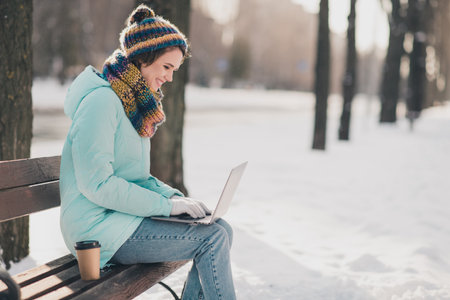 Profile side photo of attractive cheerful young woman sit bench chat laptop freezing in park...