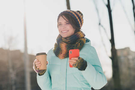 Photo of attractive happy young woman good mood smile hold phone cup takeaway coffee outdoors outside in parkの写真素材