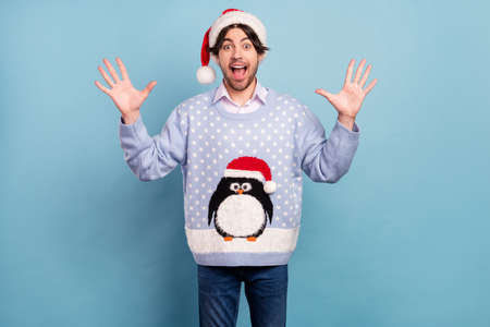 Photo of impressed cute young man dressed blue christmas pullover open mouth rising arms isolated blue color backgroundの写真素材