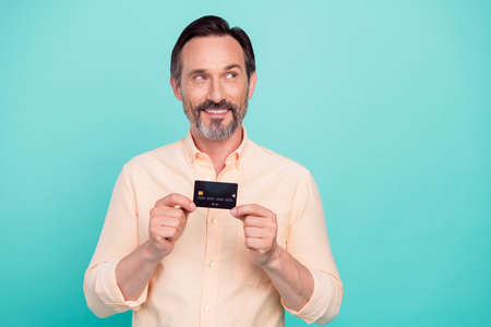 Photo of funny mature man hold card look empty space wear peach shirt isolated on teal color...