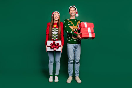 Photo of excited dream couple hold pile gifts enjoy party x-mas wear ugly sweater isolated green color backgroundの写真素材