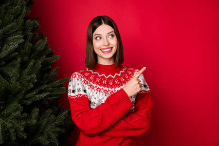 Photo of charming sweet young woman dressed print pullover looking pointing finger empty space isolated red color backgroundの写真素材