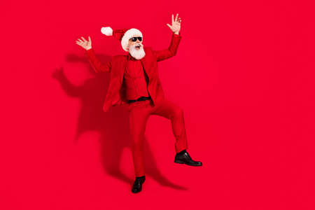 Photo of crazy careless santa claus dance look empty space wear sunglass x-mas hat suit on red color backgroundの写真素材