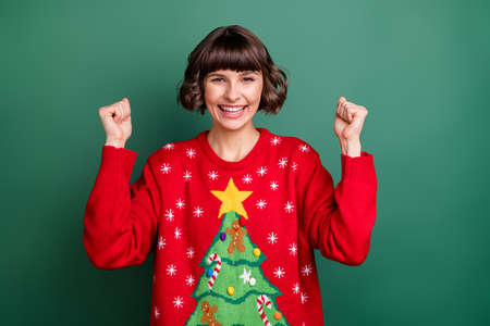 Photo of funny lucky young lady wear print sweater rising fists smiling isolated green color backgroundの写真素材