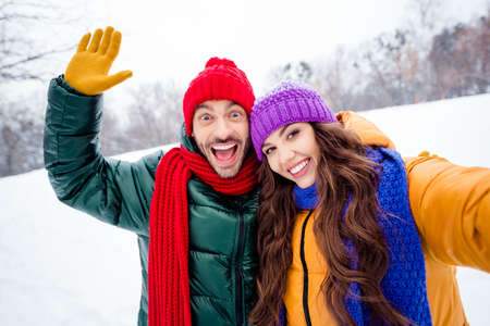 Photo of young excited couple happy positive smile make selfie wave hand hello hi vacation snowy parkの写真素材