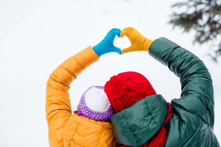 Photo of sweet adorable girlfriend boyfriend dressed vests rising hands showing fingers heart walking snow outdoors forestの写真素材