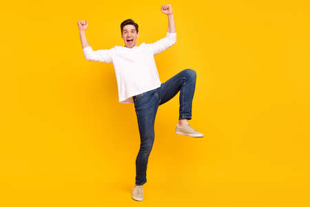 Full size photo of hooray brunet millennial guy wear shirt jeans sneakers isolated on yellow color...