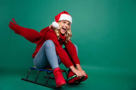 Full size profile side photo of young girl happy positive smile drive hill sledge speed fly scarf isolated over green color backgroundの写真素材