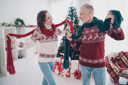 Photo of dreamy funny mature lovers wear knitted sweaters smiling holding scarves indoors house home...