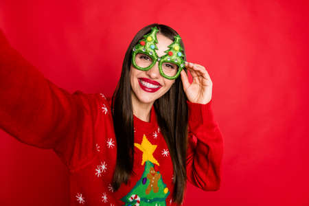 Self-portrait of attractive cheerful girl touching funny specs newyear isolated over bright red color backgroundの写真素材