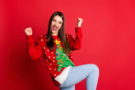 Photo of lucky funky young lady wear ornament sweater smiling rising fists isolated red color backgroundの写真素材