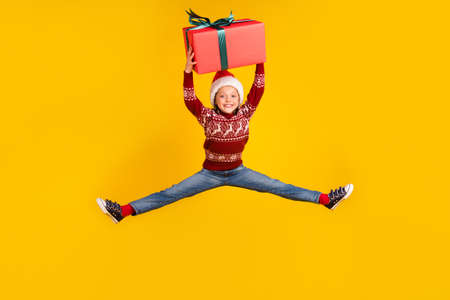 Full length photo of happy small girl hold hand present jump enjoy holiday isolated on yellow color backgroundの写真素材