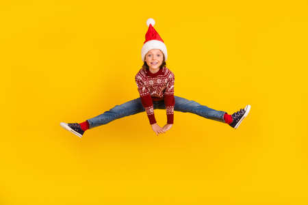 Full length photo of excited positive funky small girl jump up wear christmas clothes isolated on yellow color backgroundの写真素材