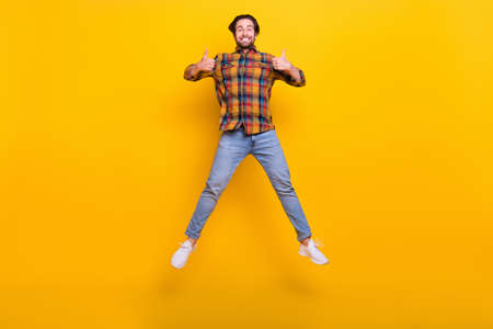 Full length photo of cool brunet millennial guy jump show thumb up wear shirt jeans sneakers...