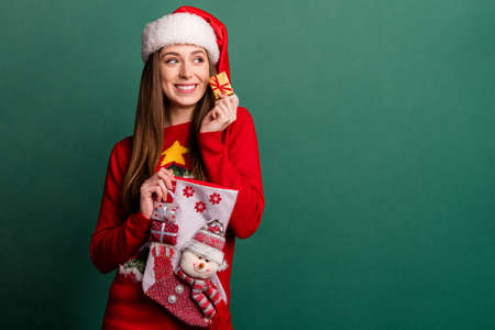 Photo of young dreamy happy positive woman look empty space hold sock small gift isolated on green...