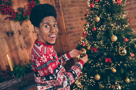 Photo of handsome cute dark skin man wear red sweater decorating christmas tree smiling indoors room home houseの写真素材