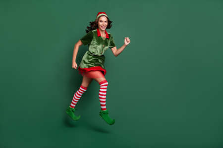 Full length body size view of attractive cheery girl Santa helper jumping running isolated over green color backgroundの写真素材