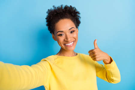 Photo of young happy joyful afro american woman make selfie thumb up smile isolated on blue color backgroundの写真素材