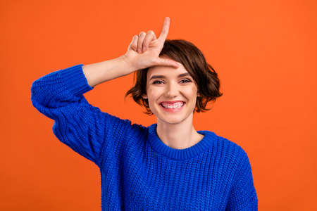 Portrait of attractive cheerful girl showing horn sign fooling bullying stupid isolated over bright orange color backgroundの写真素材