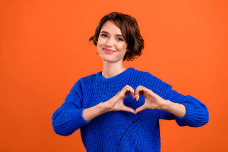 Photo of flirty brunette millennial lady show heart wear blue pullover isolated on orange color backgroundの写真素材
