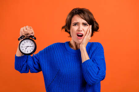 Portrait of attractive worried girl holding in hands clock bad mood late time isolated over bright orange color backgroundの写真素材
