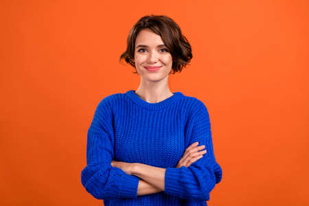 Photo of optimistic brunette hair young lady crossed arms wear blue sweater isolated on orange color backgroundの写真素材