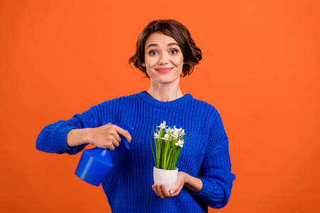 Portrait of attractive funny cheerful girl watering plant everyday care isolated over bright orange color backgroundの写真素材