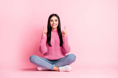 Full body portrait of positive lady sit on floor indicate fingers up empty space isolated on pink color backgroundの写真素材