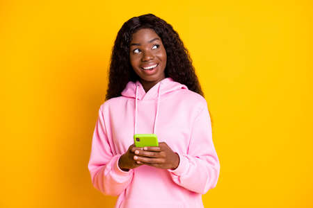 Photo of pretty dreamy dark skin lady wear pink sweatshirt typing modern device looking empty space isolated yellow color backgroundの写真素材