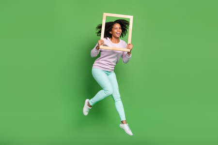 Full body photo of cool millennial brunette lady jump with frame wear pullover pants shoes isolated on blue backgroundの写真素材