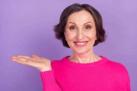 Portrait of attractive cheerful mature woman holding on palm copy space ad isolated over violet purple color backgroundの写真素材