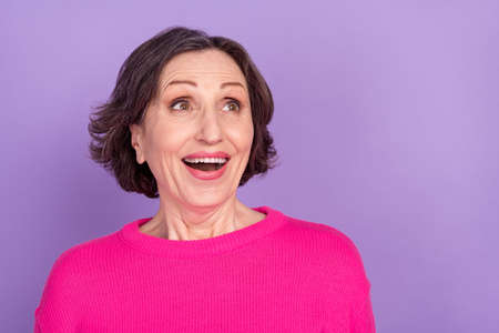 Photo of elderly woman amazed shocked excited happy positive smile look empty space isolated over violet color backgroundの写真素材