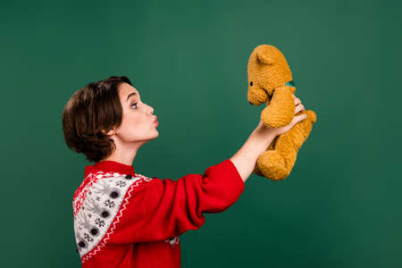 Profile side view portrait of attractive cheerful girl holding kissing old bear playing isolated over green color backgroundの写真素材