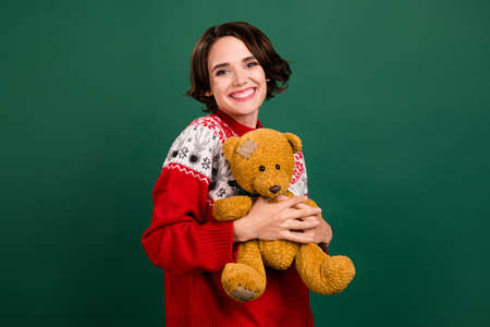Portrait of attractive cheerful girl holding hugging old bear december day isolated over green color backgroundの写真素材