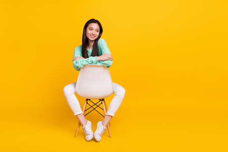 Full length photo of dreamy happy pretty woman look empty space sot chair isolated on yellow color backgroundの写真素材