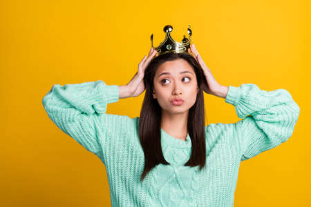 Photo of shiny dreamy young woman dressed teal pullover crown arms head looking empty space isolated yellow color backgroundの写真素材