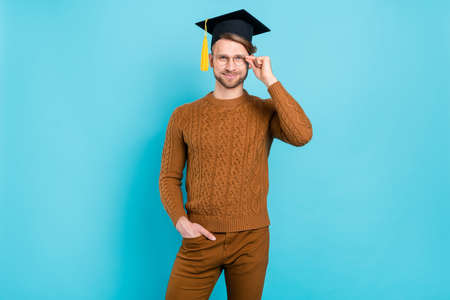 Photo of attractive young positive man wear glasses graduate hat smile isolated on blue color backgroundの写真素材