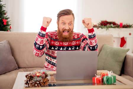 Photo of young excited man happy positive smile rejoice victory celebrate success look laptop christmas spirit indoorsの写真素材
