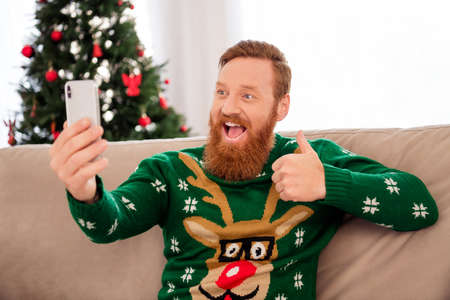 Photo of young excited man happy positive smile make selfie smartphone show thumb-up like feedback ad newyear indoorsの写真素材