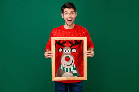 Photo portrait man in red knitted pullover on christmas smiling keeping wooden border isolated green color backgroundの写真素材